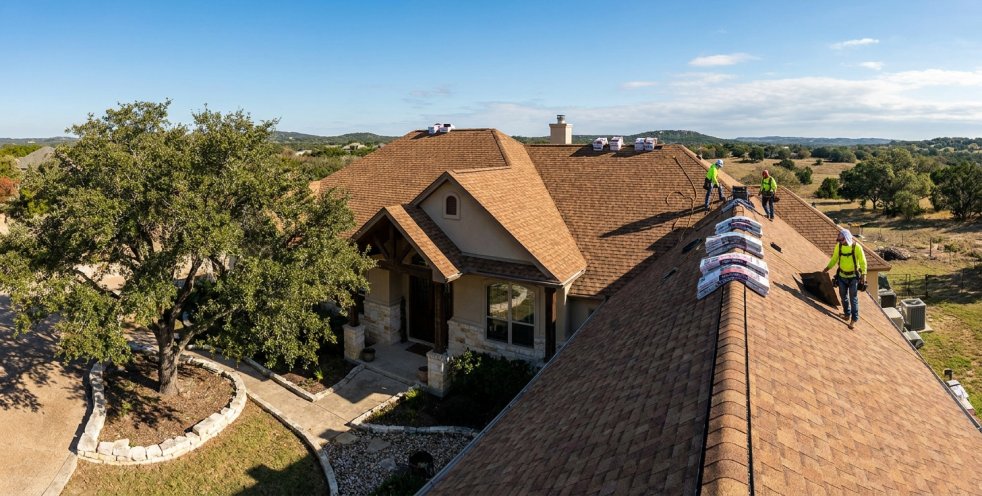 Roofing crew installing brown asphalt shingles on a home in Boerne, Texas